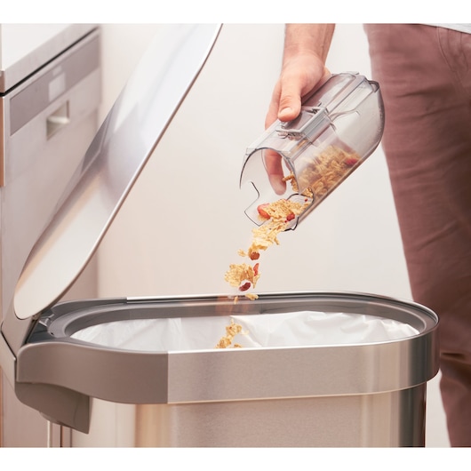 BLACKDECKER BHFEA18D1 vacuum dustbin emptied into a stainless steel trash can, side angle.