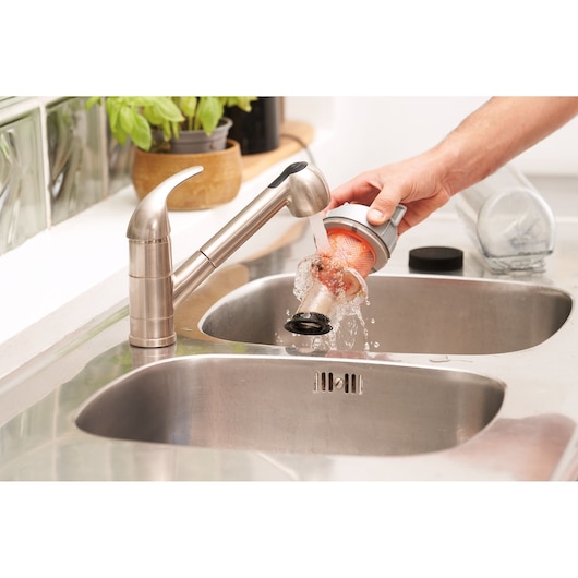 BLACKDECKER BHFEA18D1 vacuum filter being rinsed under kitchen faucet over stainless steel sink.