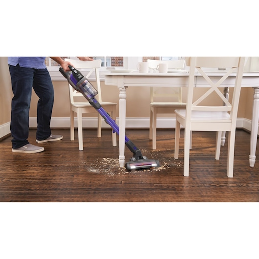 BLACKDECKER BSV20PET stick vacuum cleaning debris on hardwood floor near a dining table.
