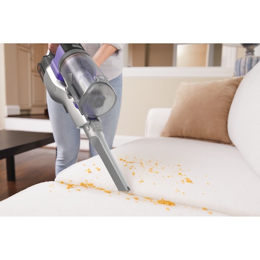 BLACKDECKER BSV20PET handheld vacuum cleaning crumbs from a white sofa in a living room.