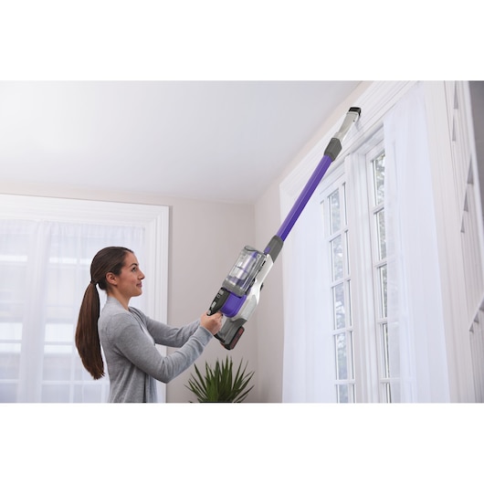 BLACKDECKER BSV20PET cordless stick vacuum in purple used to clean high window trim indoors.