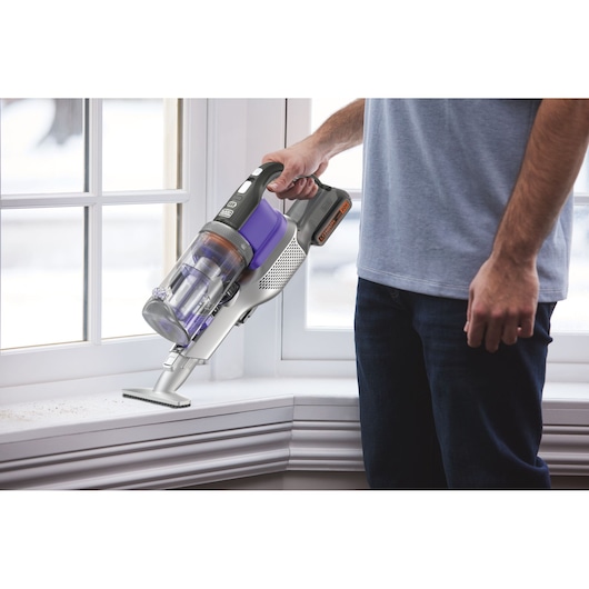 Photo of BLACKDECKER BSV20PET cordless handheld vacuum with purple and gray accents, in use cleaning a windowsill.