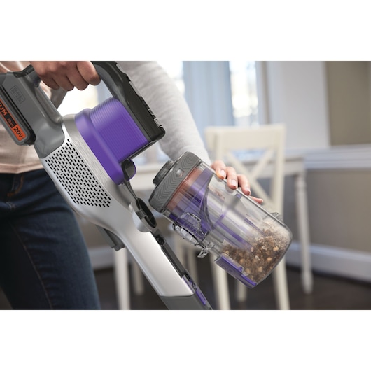 BLACKDECKER BSV20PET cordless stick vacuum with purple dustbin being emptied in a kitchen setting.
