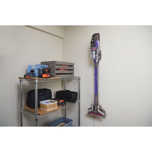 BLACKDECKER BSV20PET cordless stick vacuum mounted on a wall near metal shelving with storage boxes and tools.