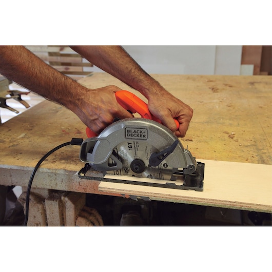 Photo of BLACKDECKER CS1004 circular saw cutting wood plank, close-up of hands guiding tool on workbench.