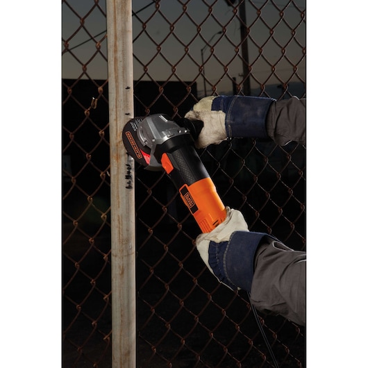Photo of BLACKDECKER G720 angle grinder being used to cut a metal pipe against a chain-link fence.