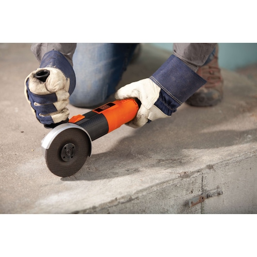BLACKDECKER G720 angle grinder held with gloves cutting concrete surface, side view.