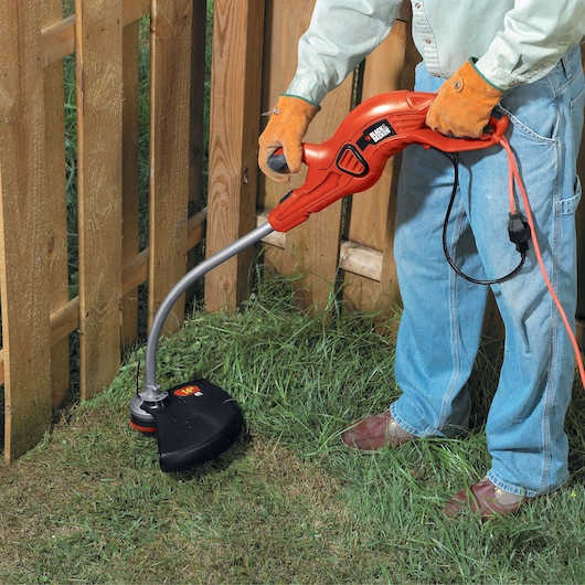 Photo of BLACKDECKER GH1100 electric string trimmer used on grass near a wooden fence.