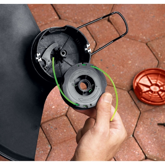 BLACKDECKER GH1100 trimmer spool and cap held by hand, green line visible, outdoor setup on tile.