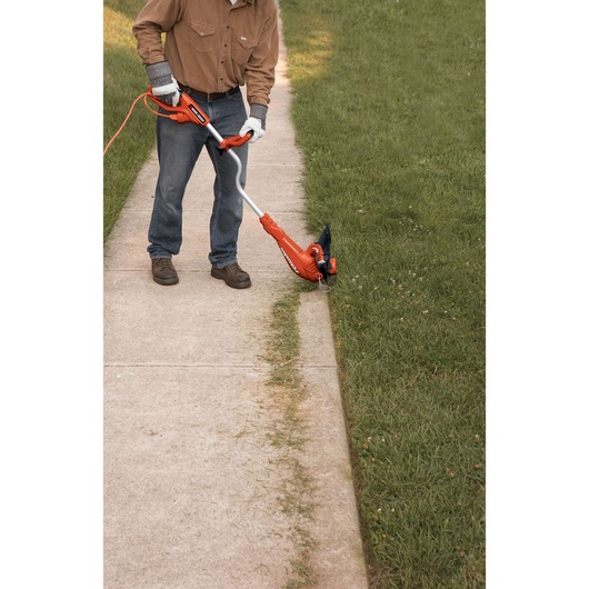 BLACKDECKER GH750 string trimmer used to edge grass along a sidewalk, photo shows tool in action outdoors.