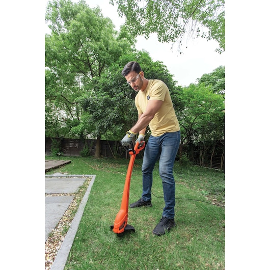 BLACKDECKER GL350 orange grass trimmer used outdoors in garden, photographed from side angle