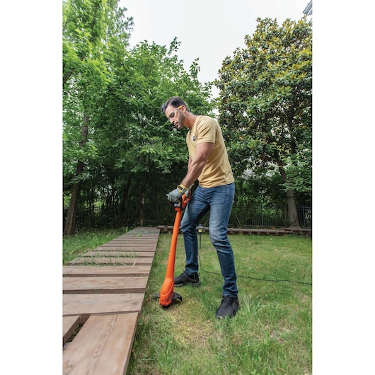 BLACKDECKER GL350 orange string trimmer in use outdoors near wooden pathway, grass, and trees.