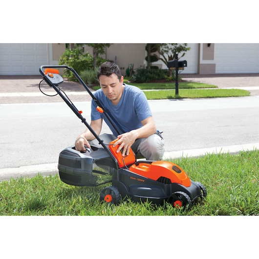 Photo of BLACKDECKER GR1000 electric lawn mower with orange and black design, shown on grass in residential area.
