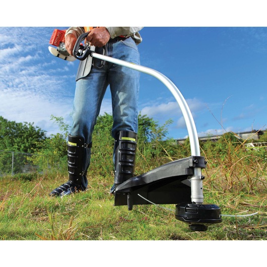 BLACKDECKER GST26 grass trimmer, close-up outdoor view, person holding handle, wearing protective boots.