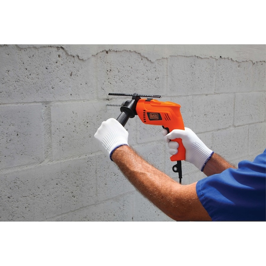 Photo of BLACKDECKER HD650 hammer drill being used on a concrete wall, held with both hands wearing white gloves.