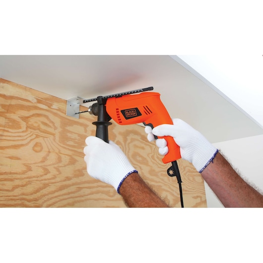 BLACKDECKER HD650 orange corded drill in use on wood panel, user wearing white gloves.