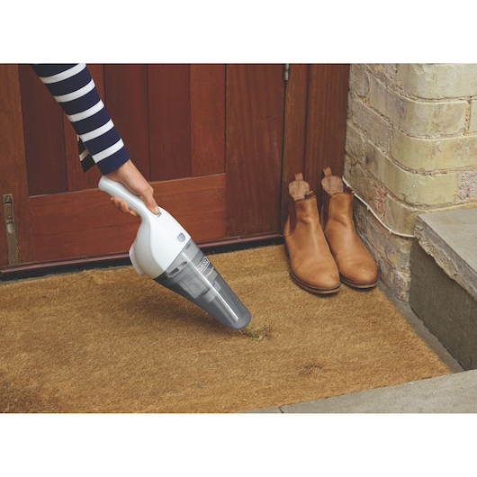 BLACKDECKER HNV220V12 handheld vacuum cleaning a brown doormat near tan boots and wooden door.