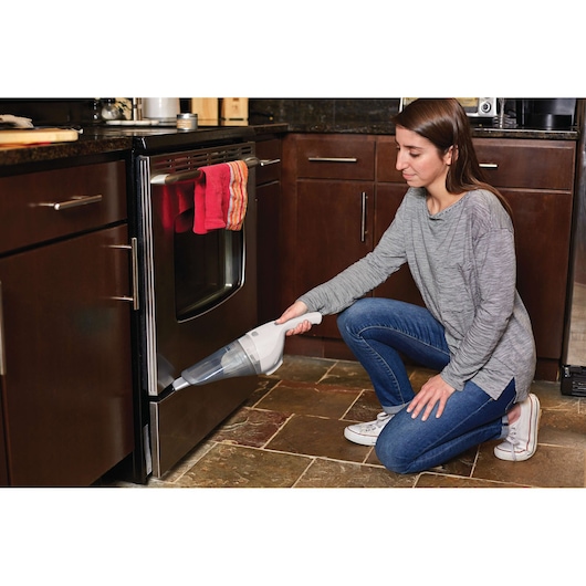 BLACKDECKER HNV220V12 handheld vacuum being used to clean kitchen floor near oven.