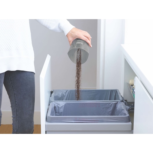 Photo of a hand emptying a BLACKDECKER HNV220V12 vacuum dustbin into a kitchen trash can.