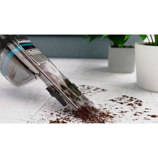 BLACKDECKER HNVD220J00 handheld vacuum cleaning dirt from a white floor, plants in the background.