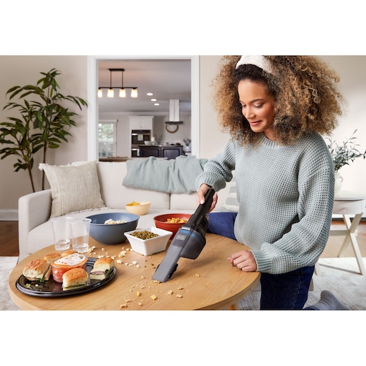 Photo of BLACKDECKER HNVD220J00 handheld vacuum cleaning crumbs from a living room table with snacks and drinks.