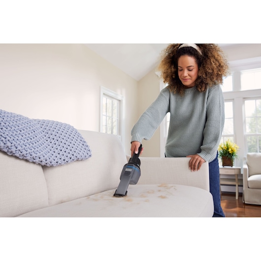 BLACK+DECKER HNVD220J00 handheld vacuum cleaning pet hair from a light-colored sofa in a living room.