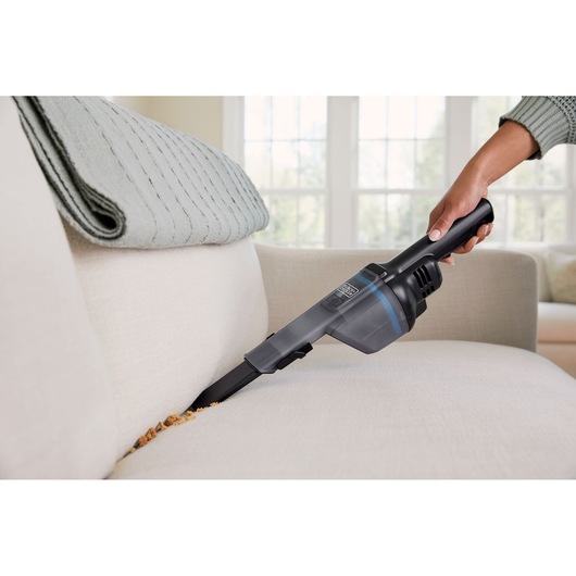BLACKDECKER HNVD220J00 handheld vacuum cleaning crumbs from a light-colored couch.