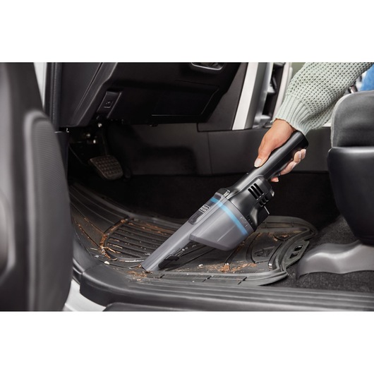 BLACKDECKER HNVD220J00 handheld vacuum cleaning dirt from car floor mat, close-up side view.
