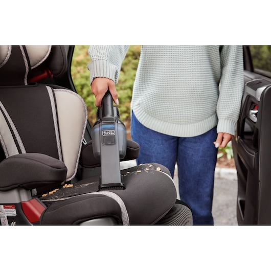 Photo of BLACKDECKER HNVD220J00 handheld vacuum cleaning crumbs from a car seat in close-up view.