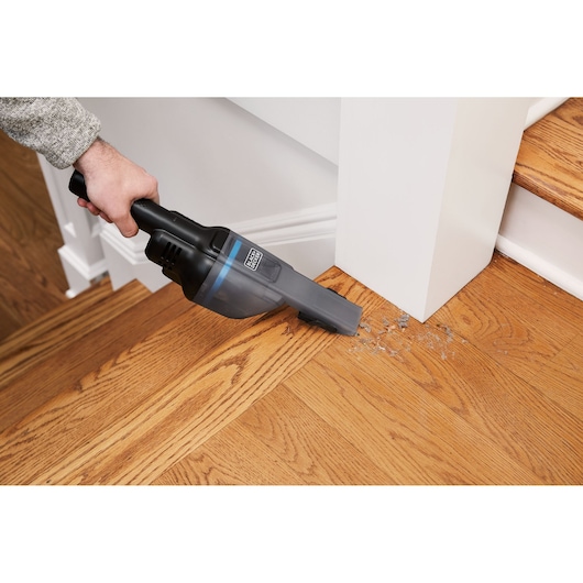 BLACKDECKER HNVD220J00 handheld vacuum cleaning debris on wood stairs, angled view.