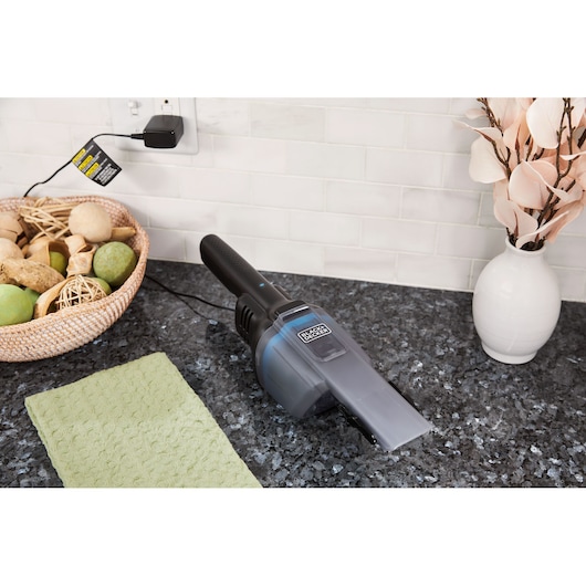BLACKDECKER HNVD220J00 handheld vacuum charging on a kitchen countertop next to a green cloth and decorative items.
