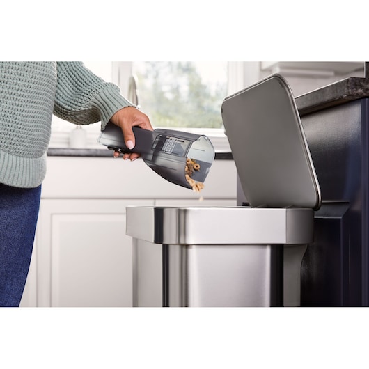 Photo of BLACKDECKER HNVD220J00 handheld vacuum being emptied into a stainless steel trash can in a kitchen.