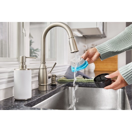 Photo of hands washing BLACKDECKER HNVD220J00 vacuum filter parts under a kitchen faucet.