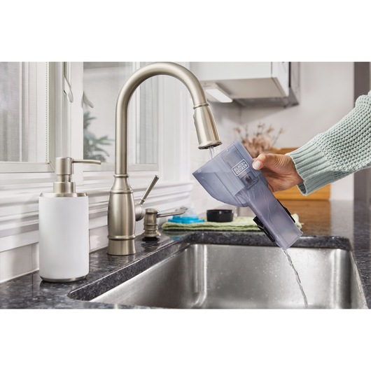 Photo of BLACKDECKER HNVD220J00 vacuum dustbin being emptied and cleaned under a kitchen faucet.