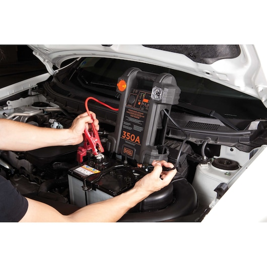 BLACKDECKER JS350S jump starter in use on a car battery, close-up photography under hood.