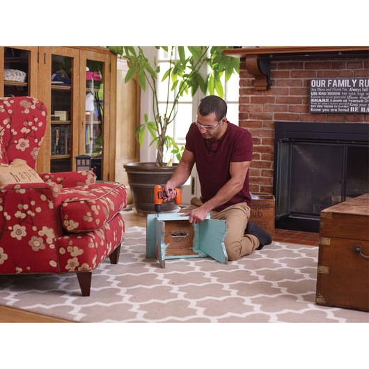 Photo of person using BLACKDECKER LD008 cordless drill to assemble a small wooden bench in a living room.