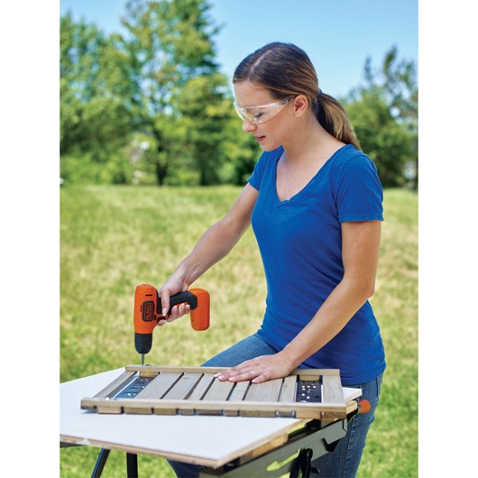 Photo of a person using a BLACKDECKER LD008 cordless drill to assemble a wooden panel outdoors.