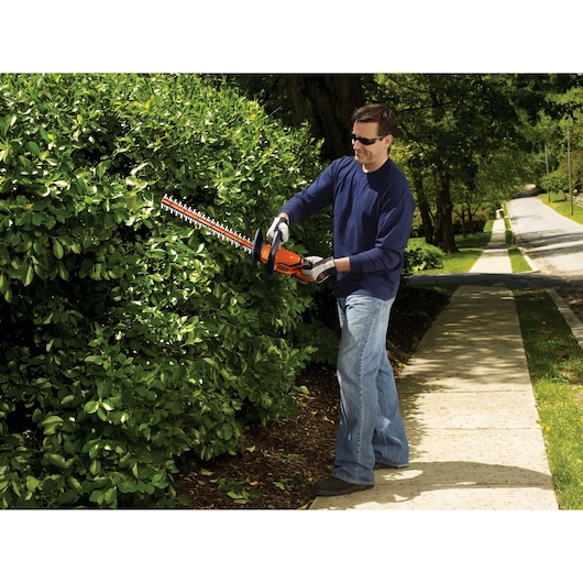 BLACKDECKER LHT2220 hedge trimmer in use cutting green bushes on a sidewalk.