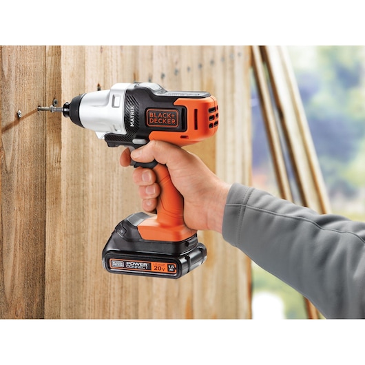 Photo of BLACK+DECKER MTX20K6A cordless drill driver in use, orange and black, driving screw into wooden surface.