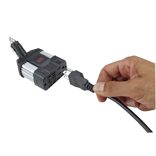 BLACKDECKER PI100LA power inverter with hand plugging in electrical cord, front angle, black and silver housing.