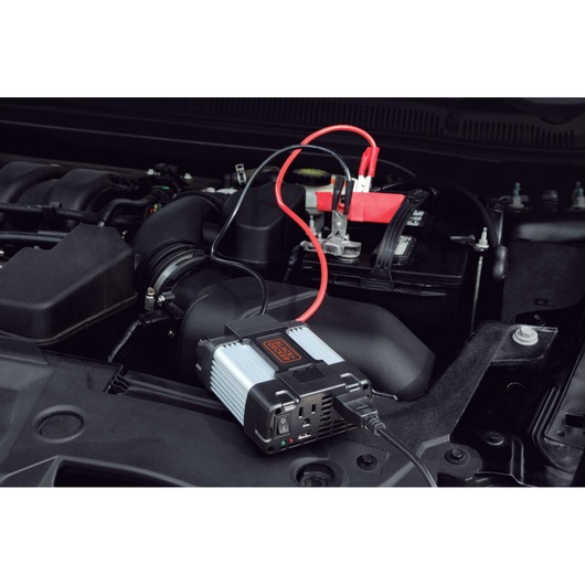 BLACKDECKER PI400LA power inverter connected to a car battery under the hood, angled side view.