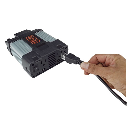 BLACK+DECKER PI750LA power inverter with hand plugging in power cord, angled view on white background.