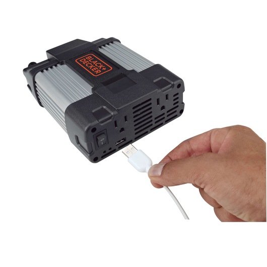 Photo of BLACK+DECKER PI750LA power inverter with a hand plugging a USB cable into the front USB port, white background.