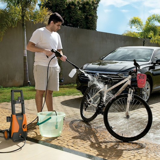 BLACKDECKER PW1450TDL pressure washer used to clean a white bicycle outdoors near a black car.