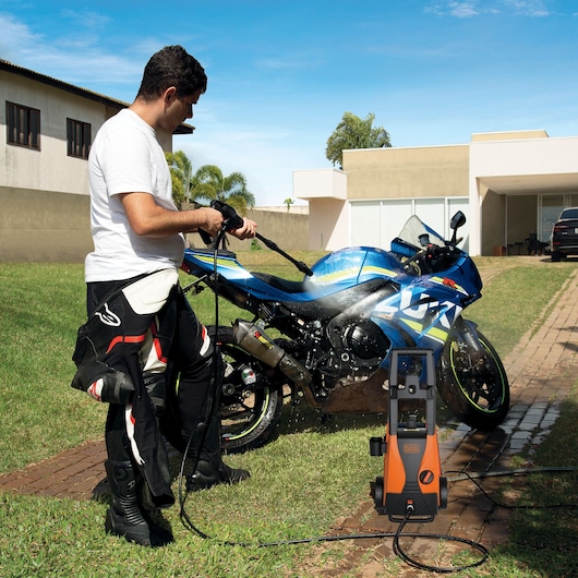 BLACKDECKER PW1450TDL pressure washer used outdoors to clean a blue motorcycle on grass.