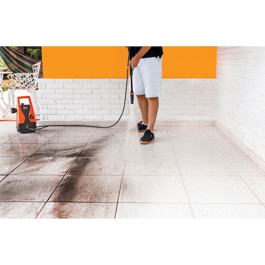 Photo of BLACKDECKER PW1450TD pressure washer cleaning dirty tiled floor, orange and white colors, side angle.