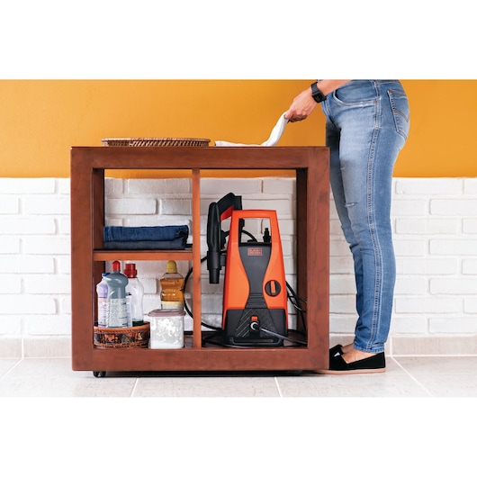 Photo of BLACKDECKER PW1450TD pressure washer stored on shelf with cleaning supplies, partial person standing nearby.