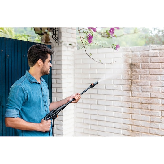 BLACKDECKER PW1450TD pressure washer cleaning a white brick wall outdoors, held by a person.