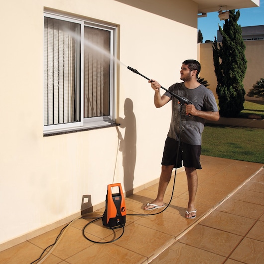 BLACKDECKER PW1450TD pressure washer in use cleaning a window outdoors, showing water spray and compact design.