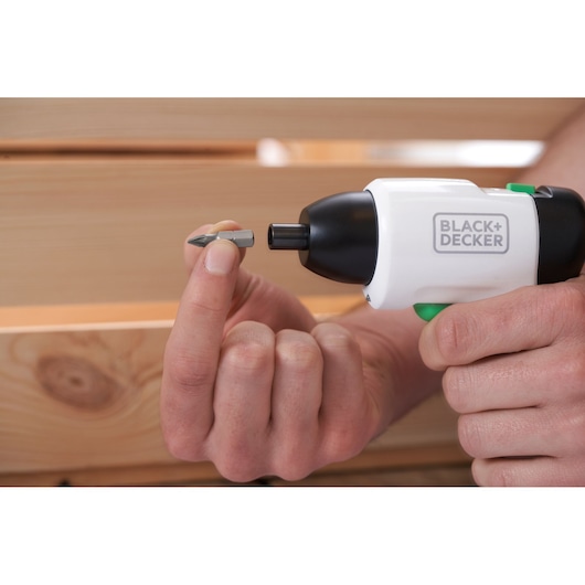 Photo of BLACK+DECKER REVSD4C cordless screwdriver, close-up of hand inserting bit, wooden background.
